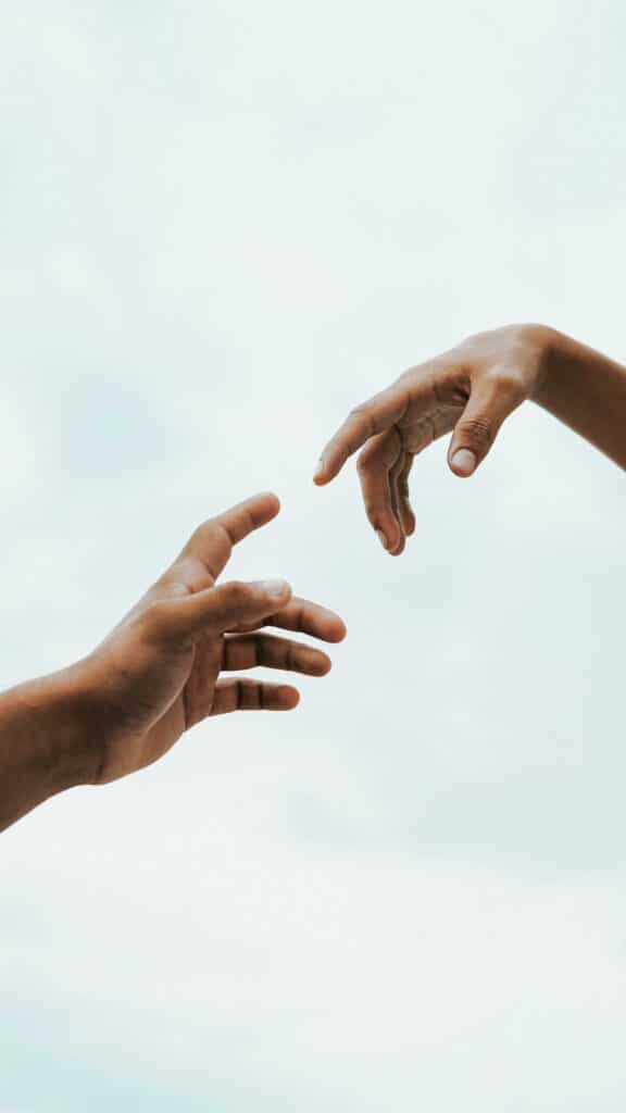 Two hands reaching toward each other against a bright sky, symbolizing connection and unity.